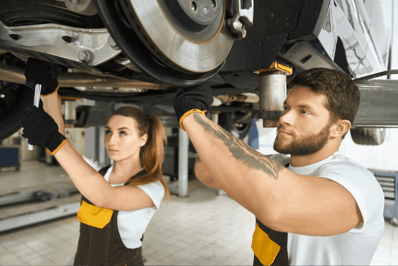 Man and woman mechanics repairing car undercarriage.<br />
